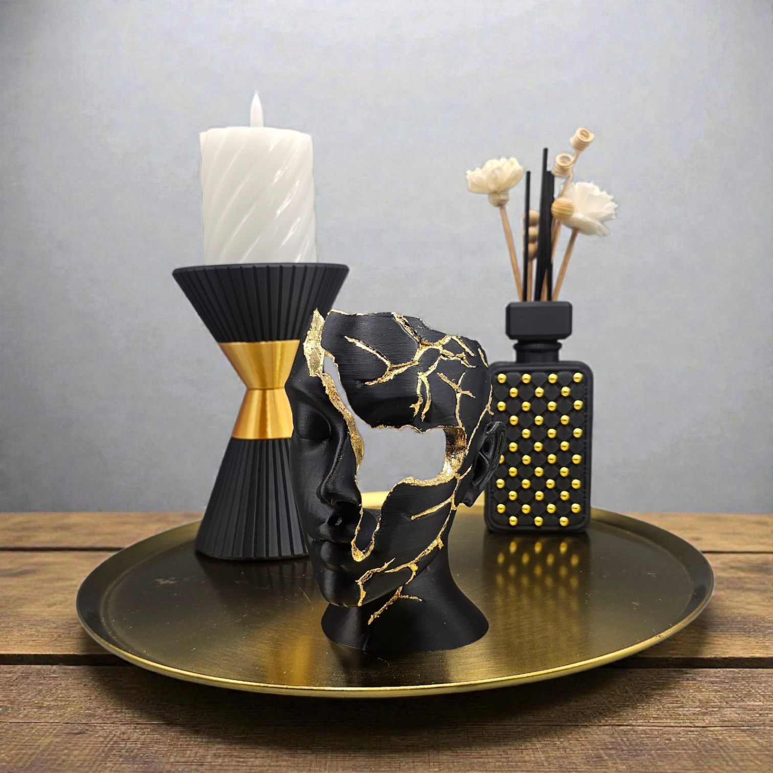 Een zwart-gouden, zandlopervormige decoratieve vaas naast een klein glazen flesje op een marmeren ondergrond met maataanduidingen.