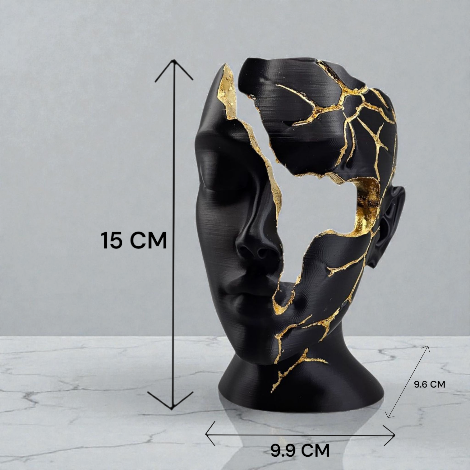 Een zwart, artistiek hoofdbeeld met met goud gevulde barsten, 15 cm hoog en 9,9 cm breed, geplaatst op een wit marmeren oppervlak.