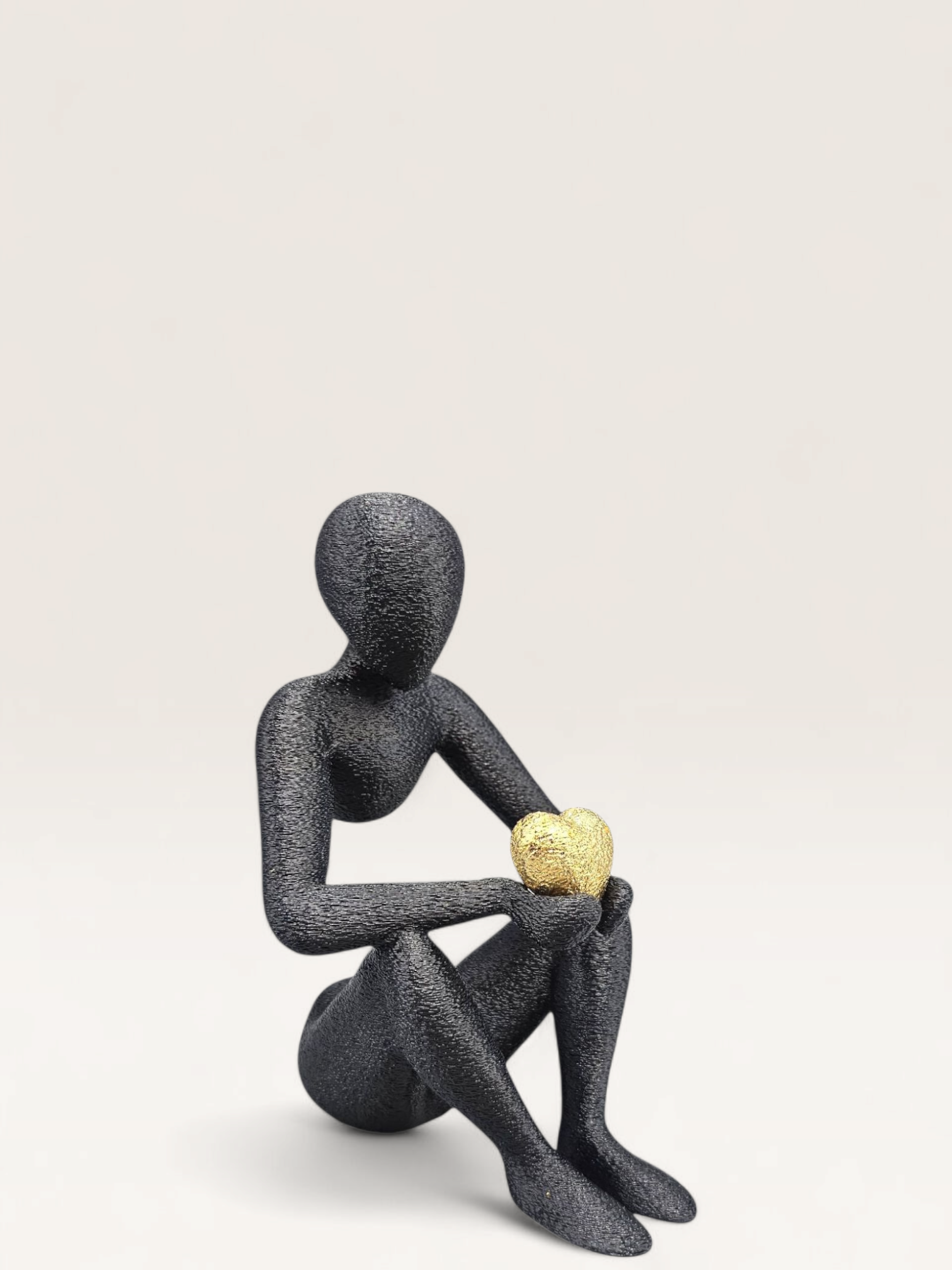 Een abstracte, zwarte figuur met textuur staat op een marmeren ondergrond en houdt een gouden hart vast. De afmetingen zijn 15x10,5x9,5 cm.