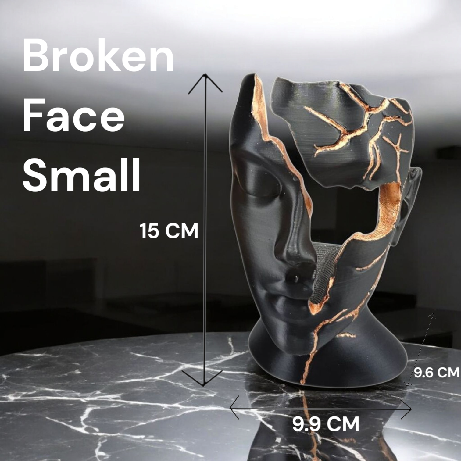 Een zwart, gebroken gezichtsculptuur met met goud gevulde barsten, 15 cm hoog, staand op een donkere ondergrond met marmerpatroon.
