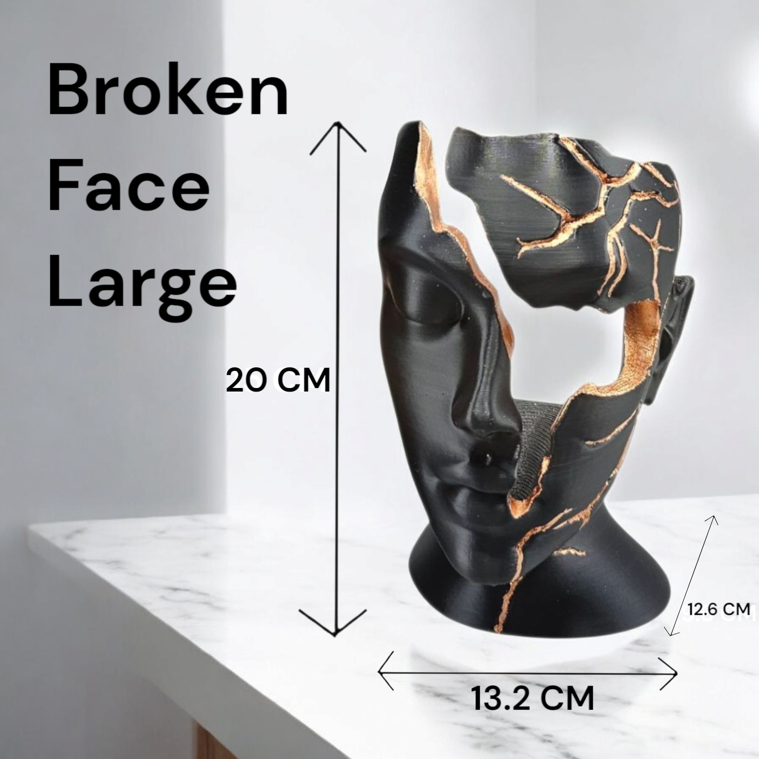 Een zwart, gebroken gezichtsculptuur met met goud gevulde barsten, 15 cm hoog, staand op een donkere ondergrond met marmerpatroon.