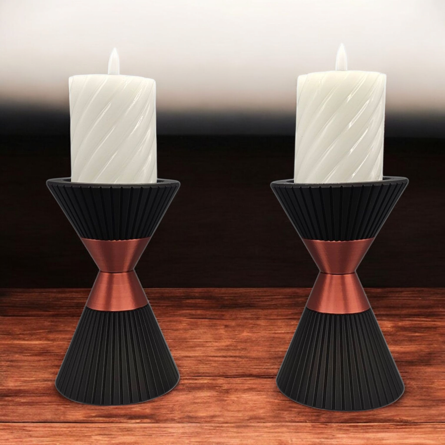 Twee witte kaarsen in decoratieve, zwarte en koperkleurige, zandlopervormige houders, staan op een houten ondergrond.