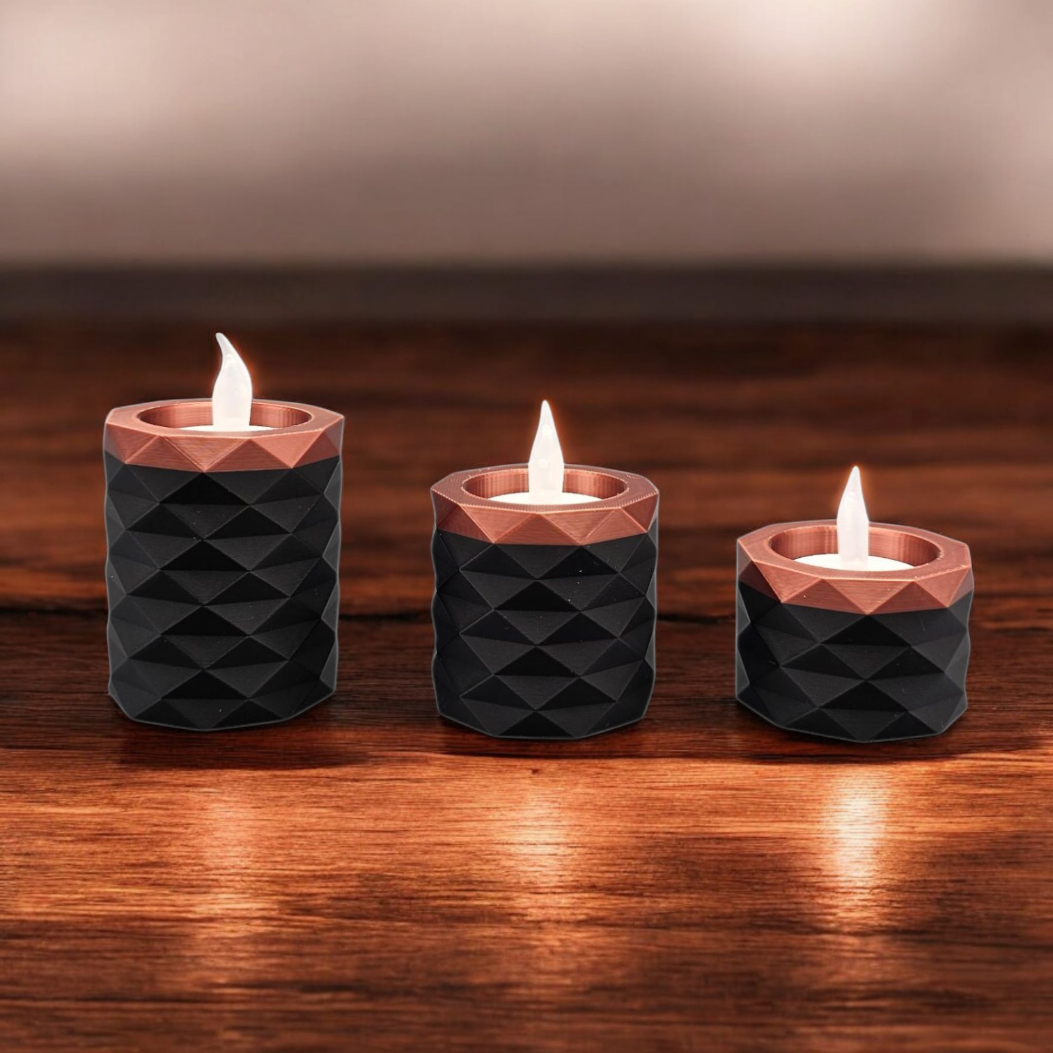 Drie zwarte, geometrisch vormgegeven kaarsenhouders met koperen randen, elk met een brandend LED-theelichtje op een houten ondergrond.