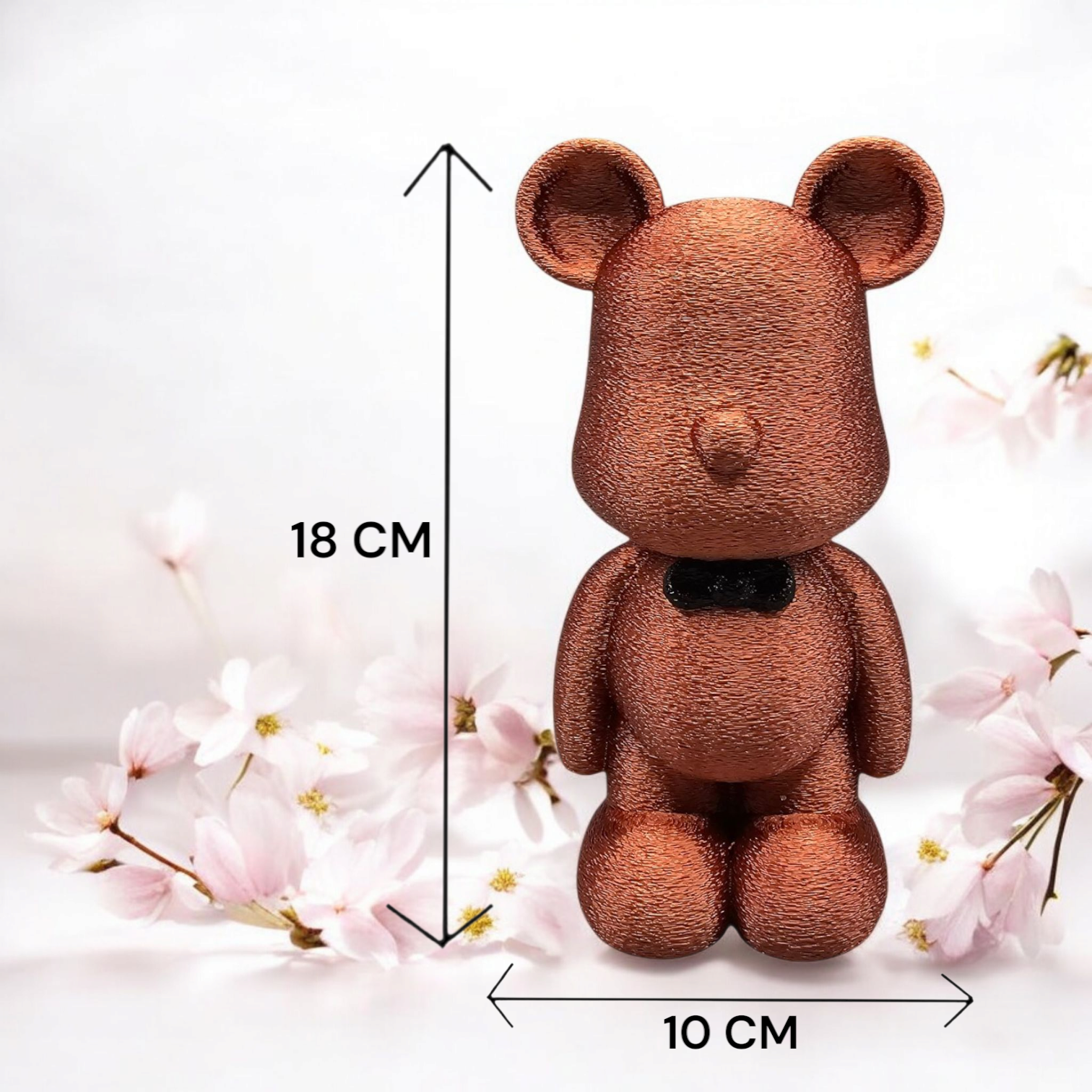 Een gestructureerd, bronskleurig berenbeeldje met een vlinderdasje, 18 cm hoog en 10 cm breed, omringd door kersenbloesems.