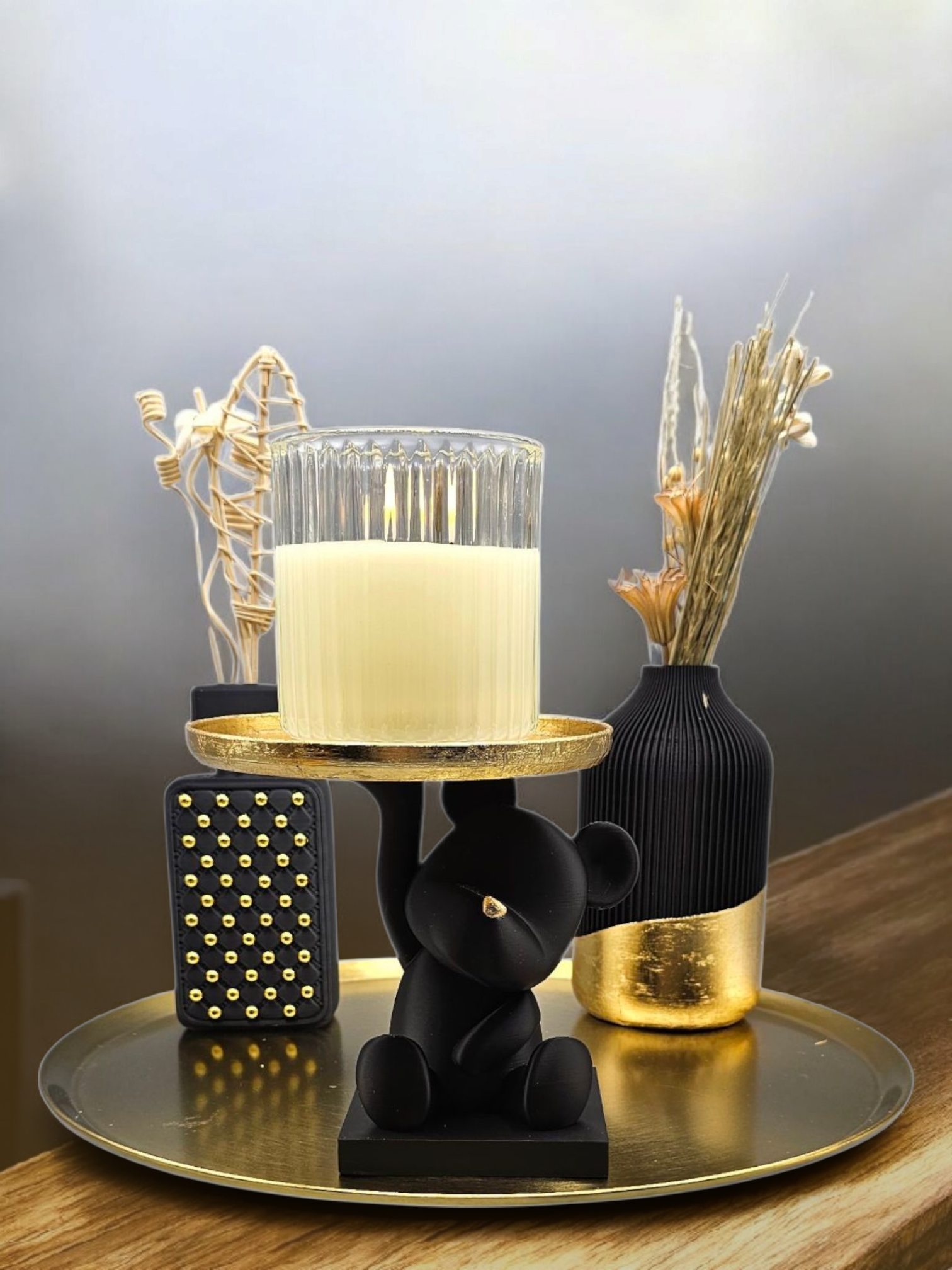 Een beeldje van een zwarte beer houdt een kaarsenplateau vast op een gouden schaal, geflankeerd door twee decoratieve vazen met gedroogde bloemen.