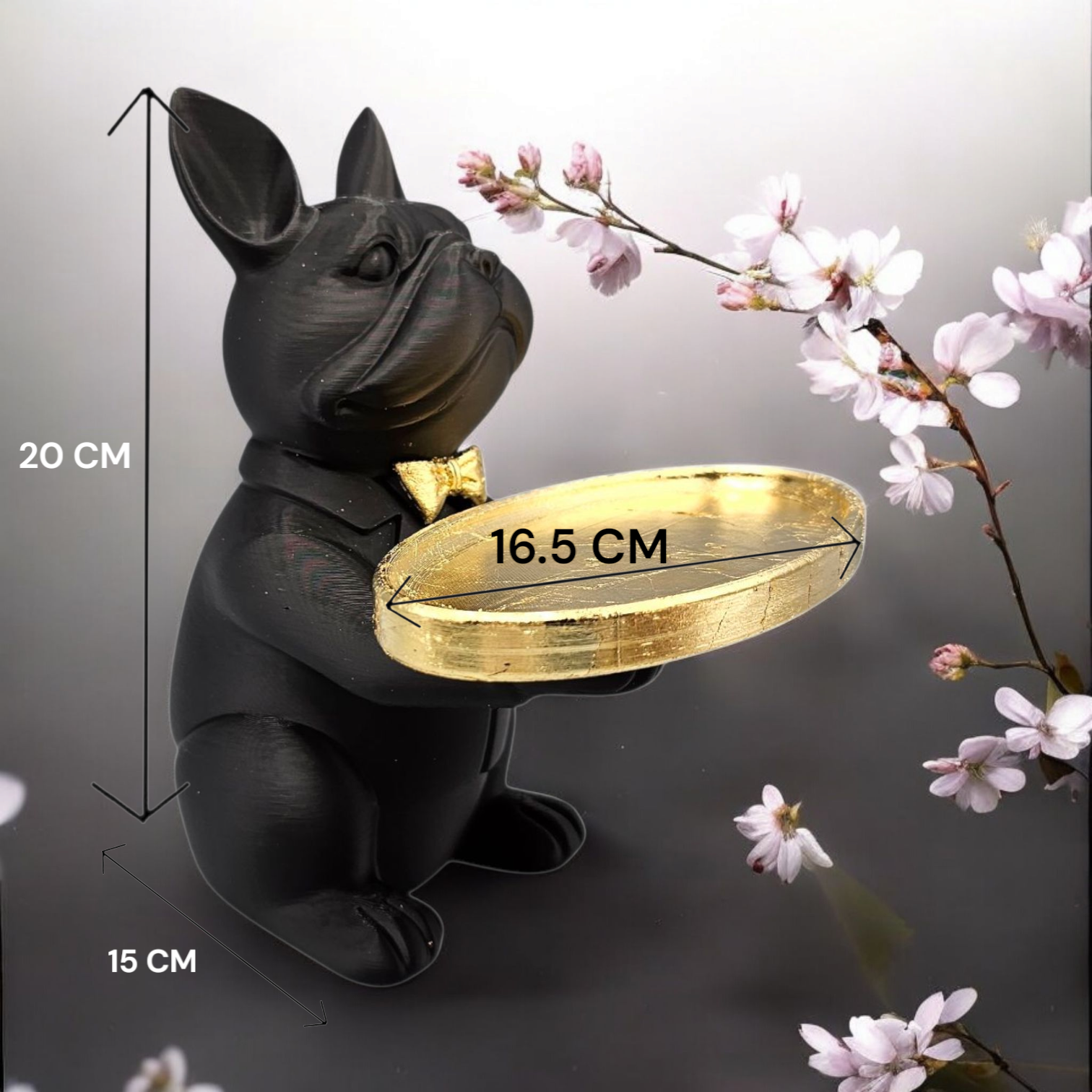 Een beeldje van een zwarte Franse bulldog met een gouden strik en een gouden dienblad, geplaatst tegen een achtergrond van kersenbloesems.