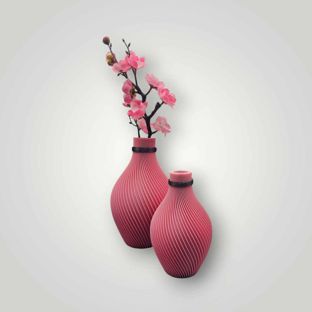 Twee vazen met een structuur in magentakleur staan naast elkaar, in één ervan staat een delicate tak met roze bloesem tegen een grijze muur.