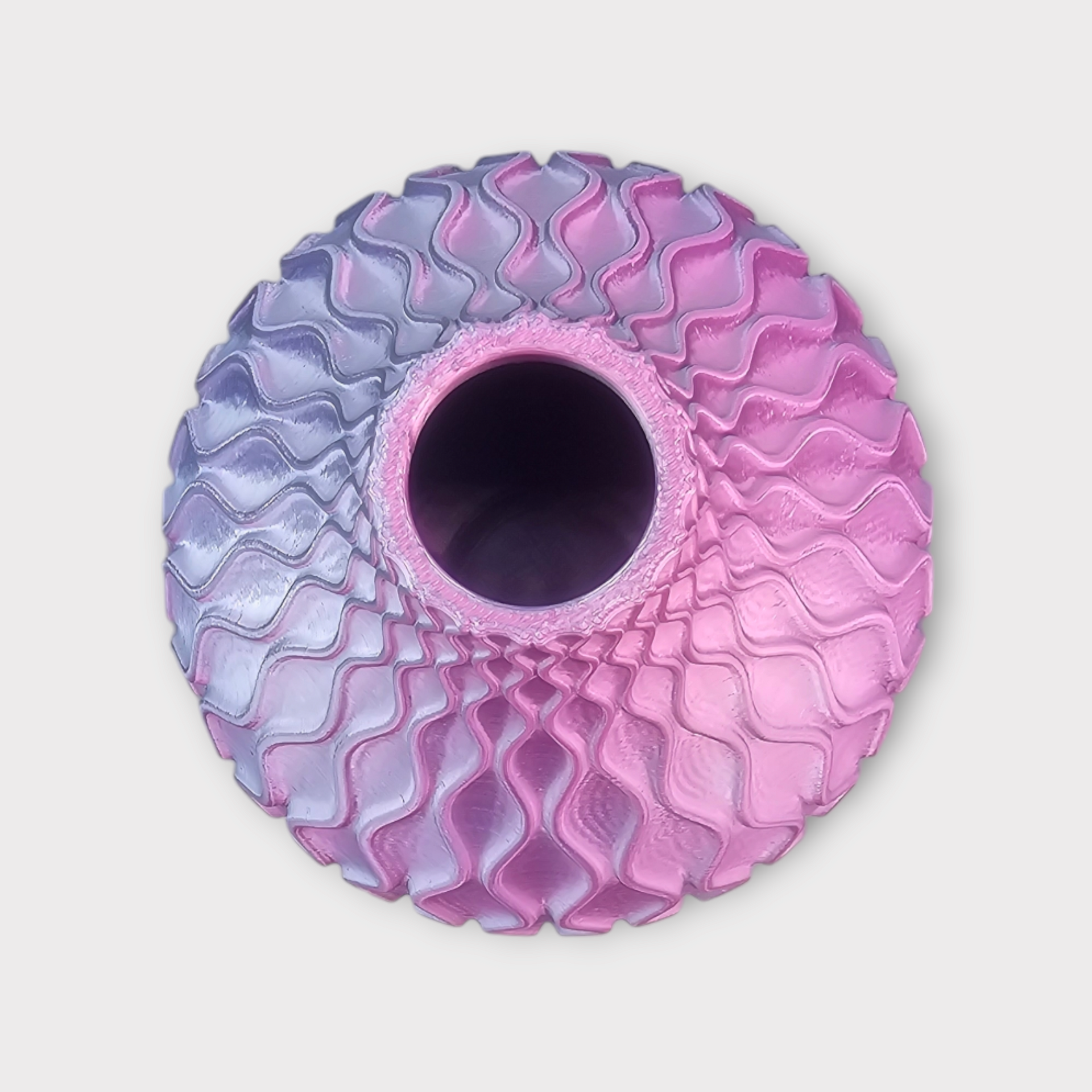 Een bovenaanzicht van een bolvormige, 3D-geprinte vaas met een golvende honingraatstructuur die van blauw naar roze overgaat.