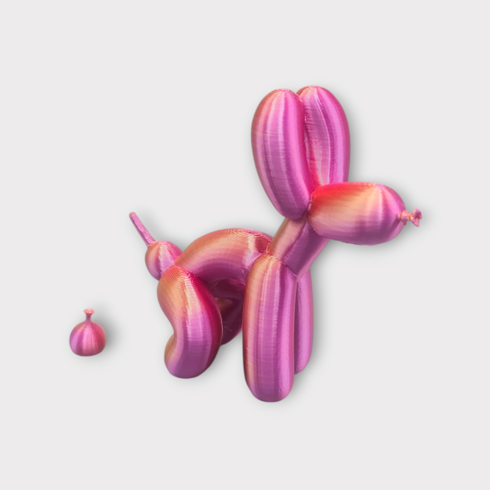 Een glanzende, metallic roze ballonhond die lijkt te poepen uit een kleine, ronde ballon.
