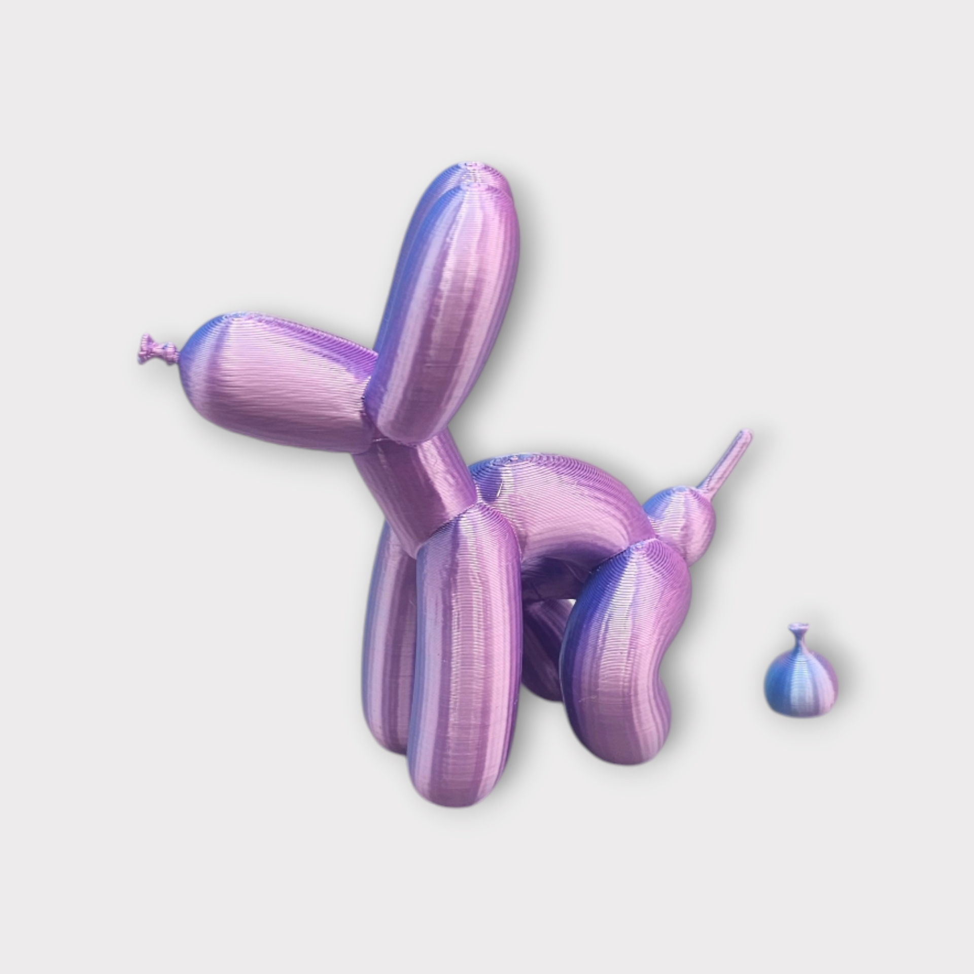 Een glanzende, metallic roze ballonhond die lijkt te poepen uit een kleine, ronde ballon.
