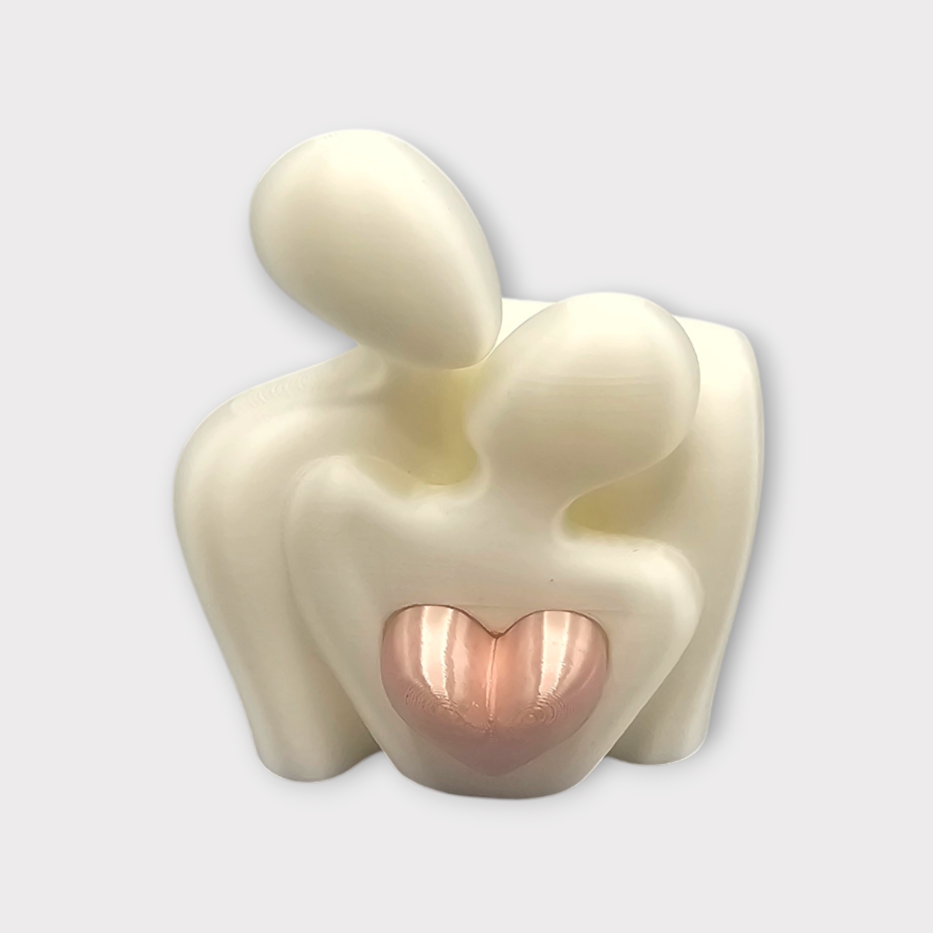 Een gladde, gebroken witte abstracte sculptuur van twee omhelzende figuren, met in het midden een metallic roségoudkleurig hart.