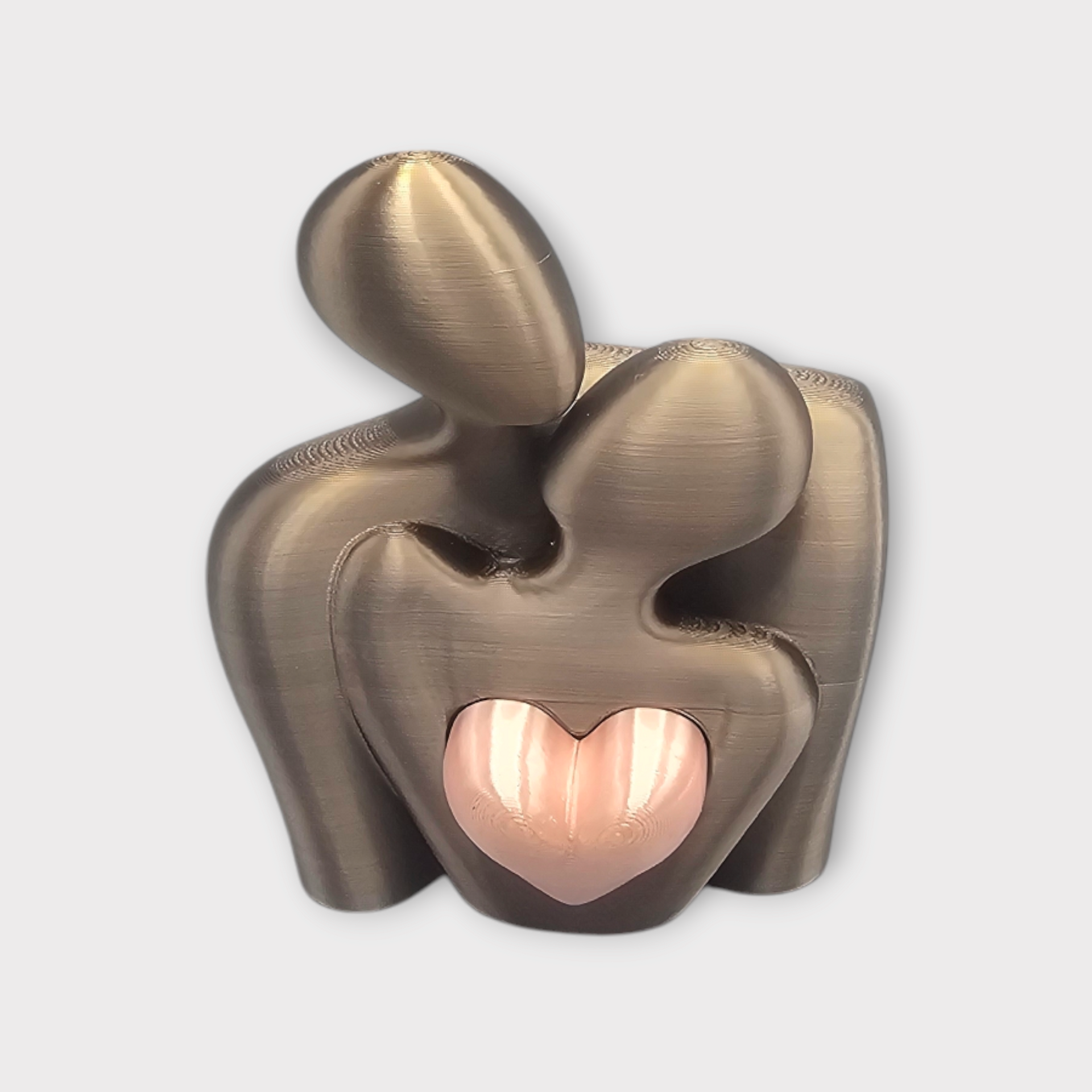 Een gladde, gebroken witte abstracte sculptuur van twee omhelzende figuren, met in het midden een metallic roségoudkleurig hart.