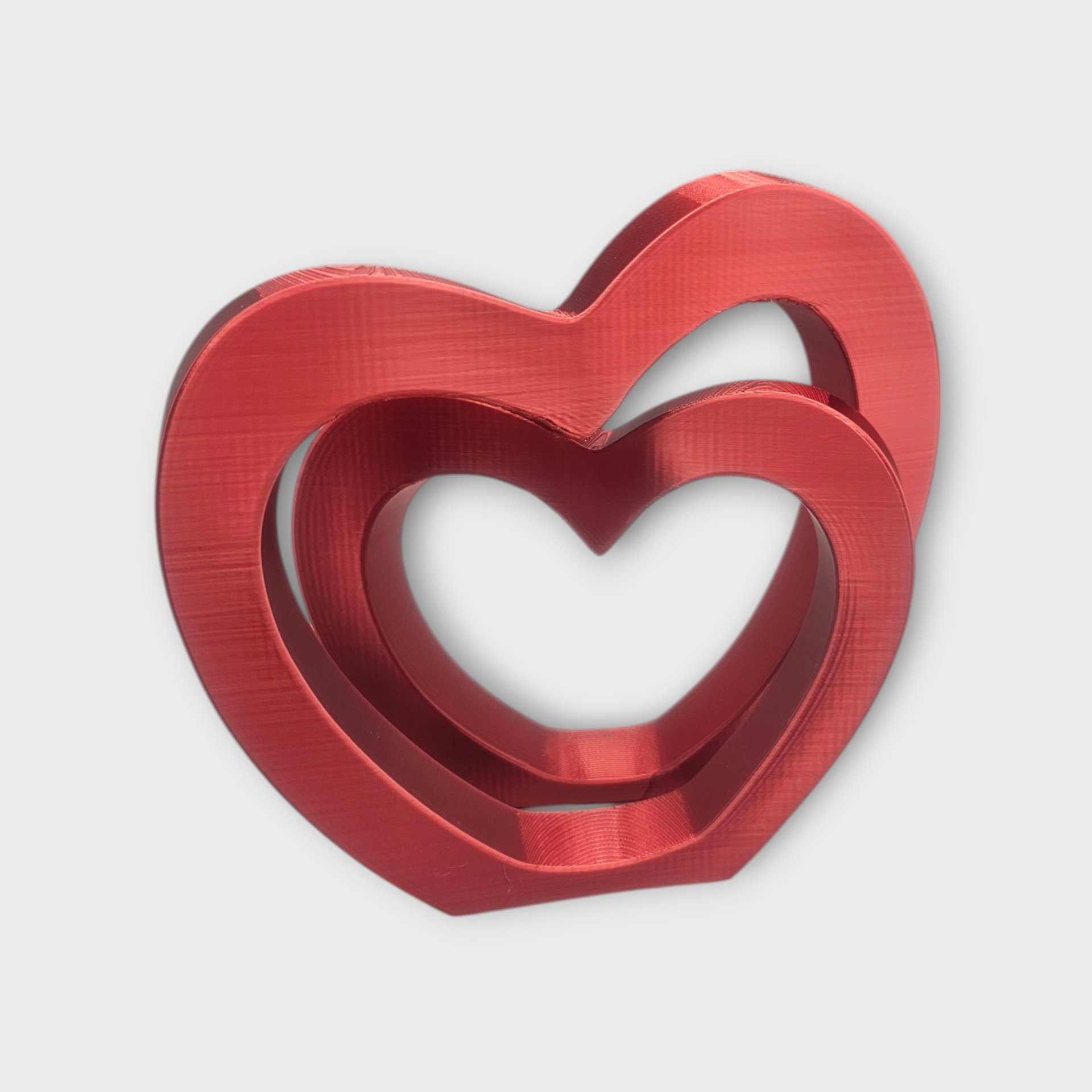 Een metallic rood 3D-geprint ornament met twee in elkaar grijpende hartvormen.