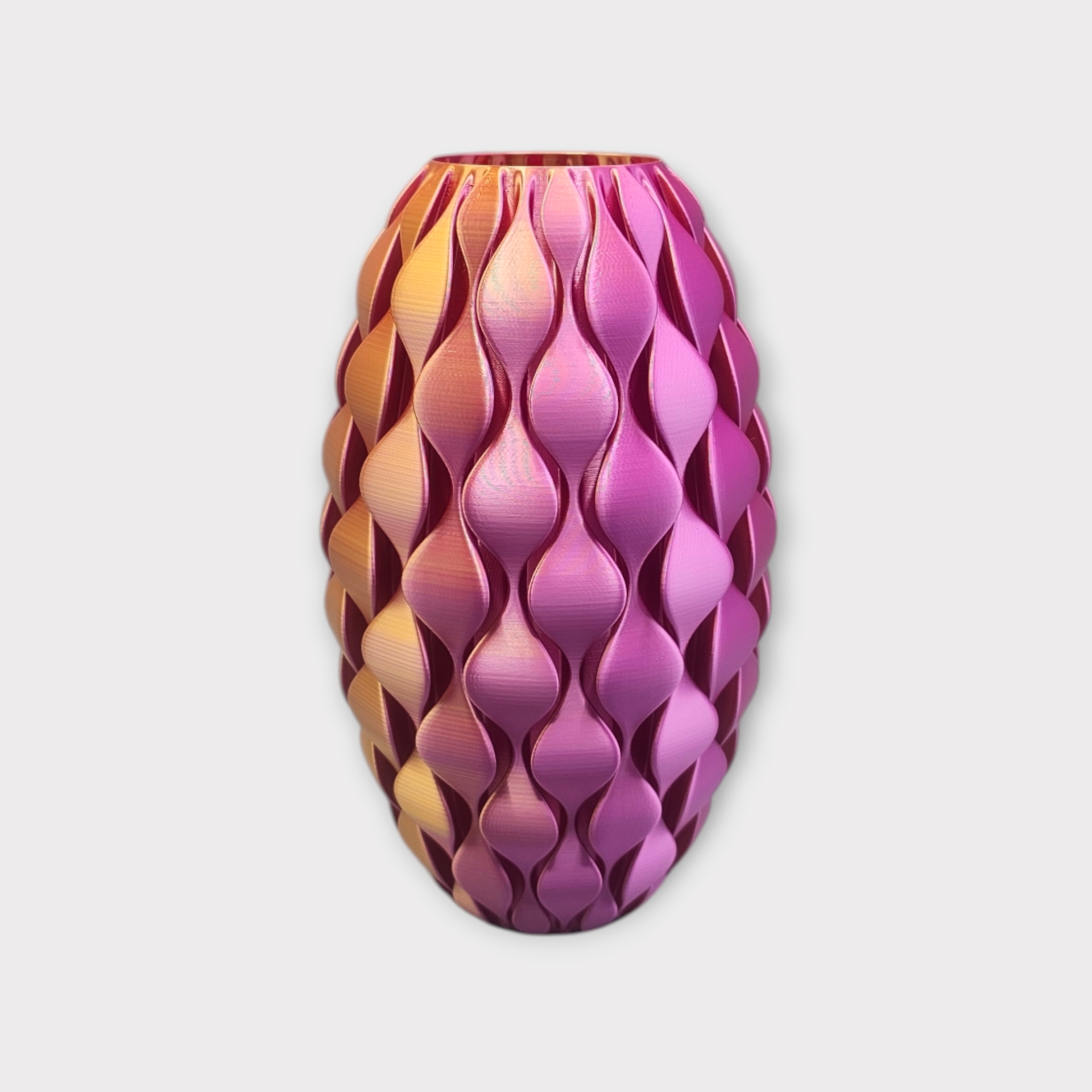 Een ovale, 3D-geprinte vaas met een gestructureerd, herhalend golfpatroon, met een kleurverloop van goud naar roze.