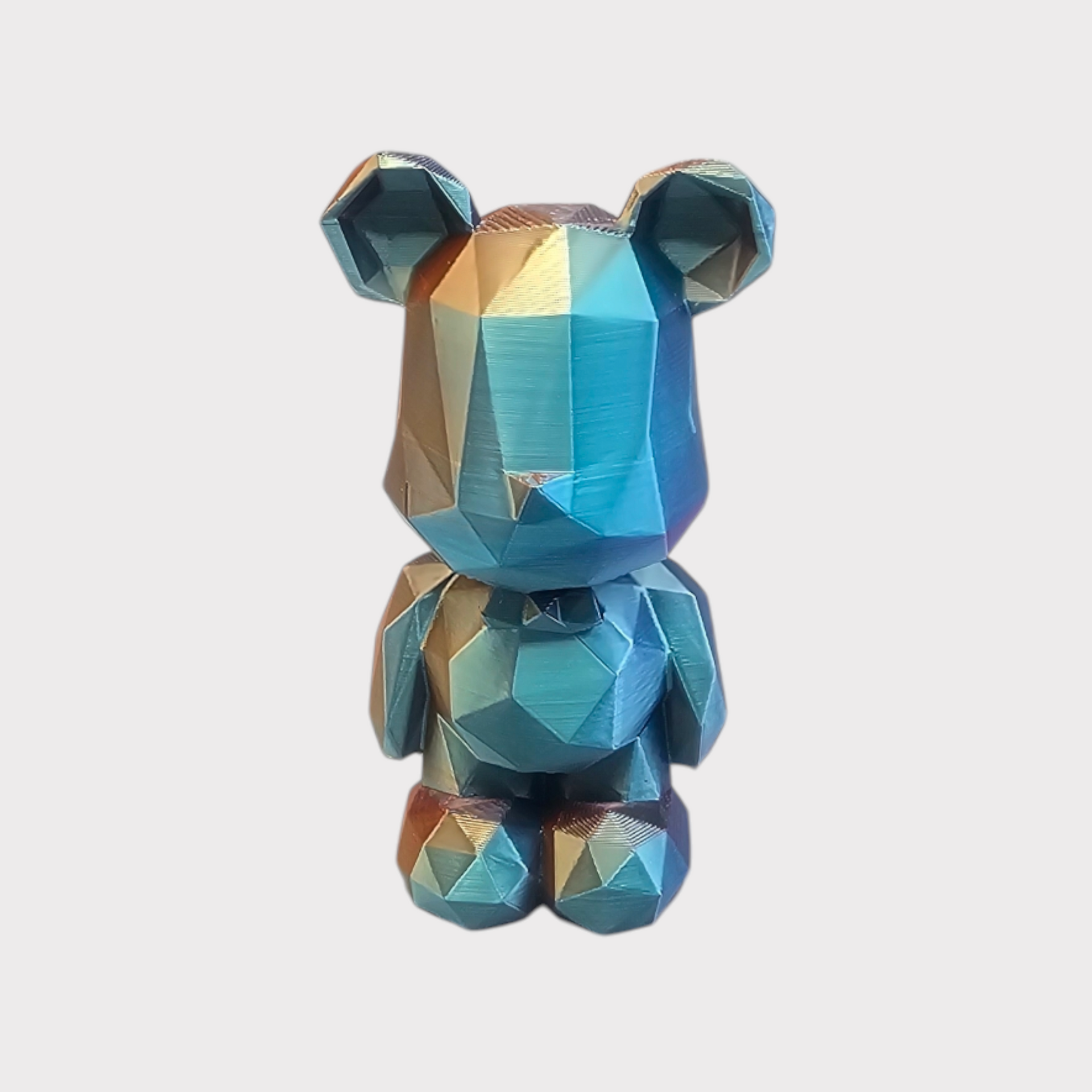 Een low-poly, geometrisch beeldje van een gestileerde beer met een metallic, iriserende blauw-gouden afwerking.