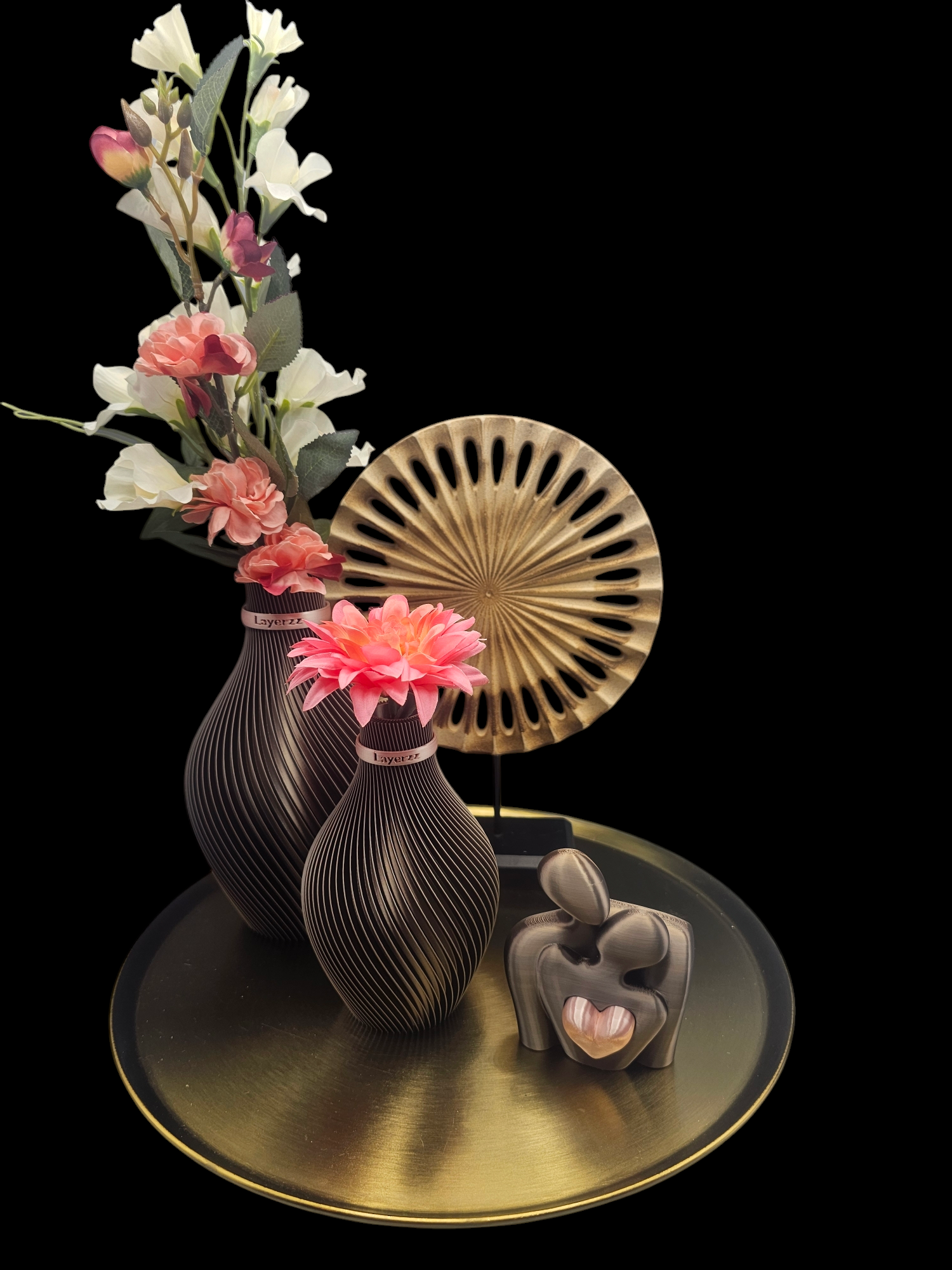 Decoratief arrangement op een gouden dienblad: vazen met bloemen, een waaiervormig ornament en een sculptuur van omhelzende figuren.