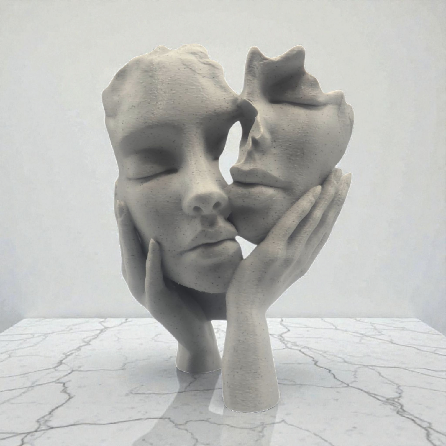 Een sculptuur met steenstructuur van twee gezichten die door handen worden vastgehouden, tentoongesteld op een wit marmeren oppervlak tegen een witte achtergrond.