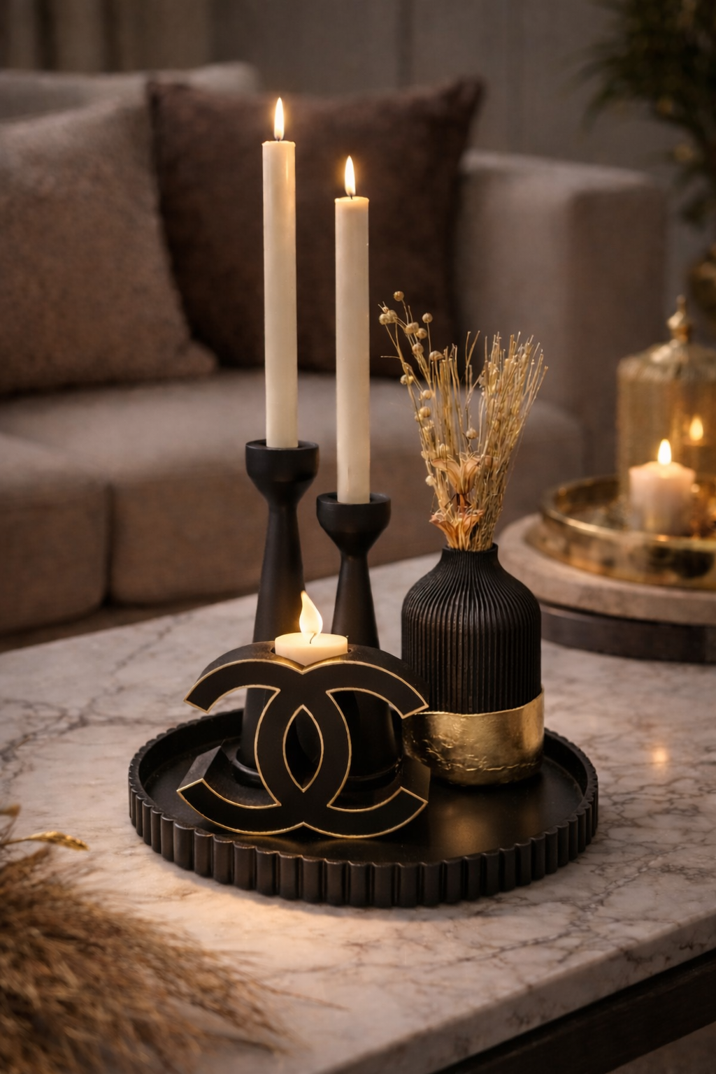 Op een marmeren tafel staat een zwart, decoratief dienblad met twee hoge kaarsen, een klein vaasje met gedroogde bloemen en een logo-item.