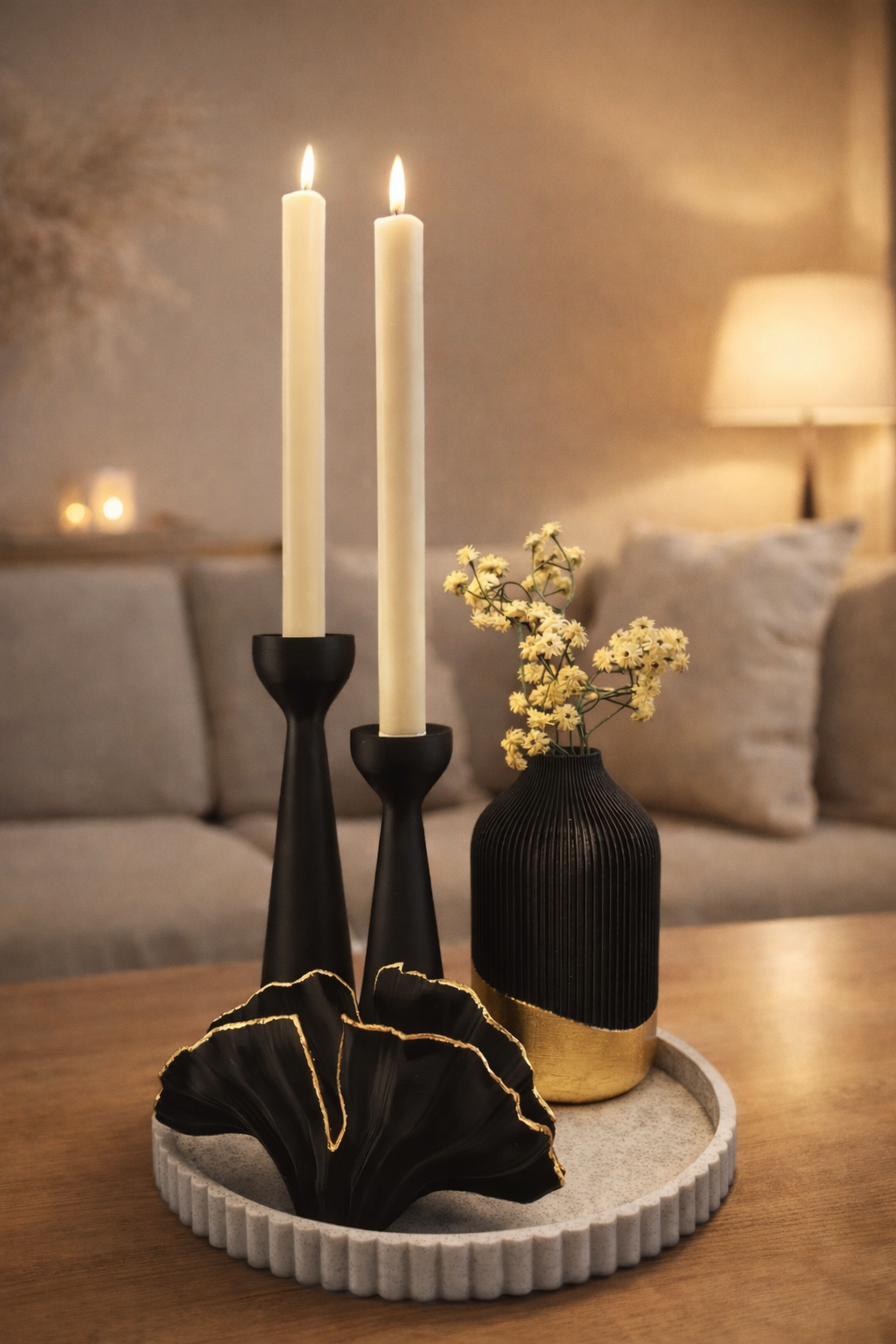 Een dienblad met structuur waarop twee zwarte kaarsen staan, een kleine zwart-gouden vaas met gele bloemen en een zwart beeldje.