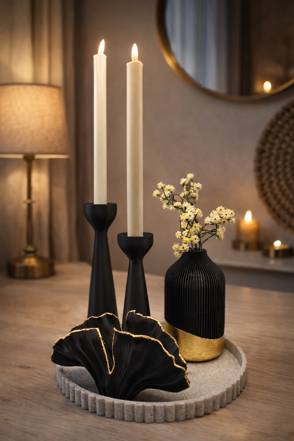 Een dienblad met structuur waarop twee zwarte kaarsen staan, een kleine zwart-gouden vaas met gele bloemen en een zwart beeldje.