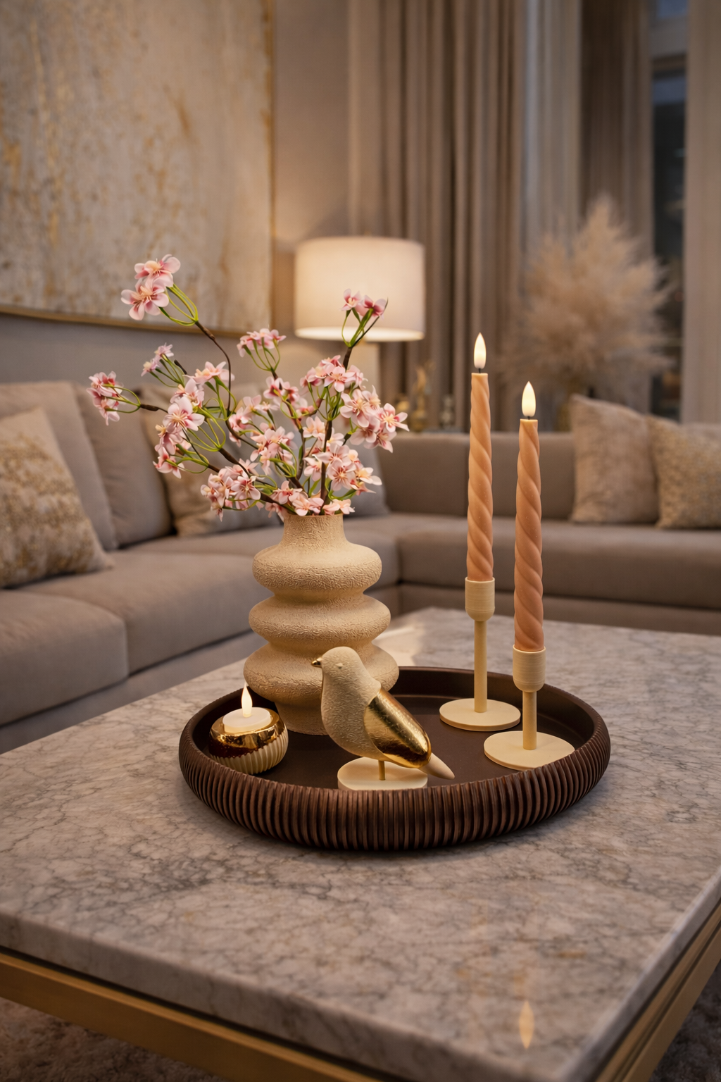 Op een decoratief dienblad op een marmeren tafel staan een vaas met kersenbloesems, twee smalle kaarsen en een vogelbeeldje.