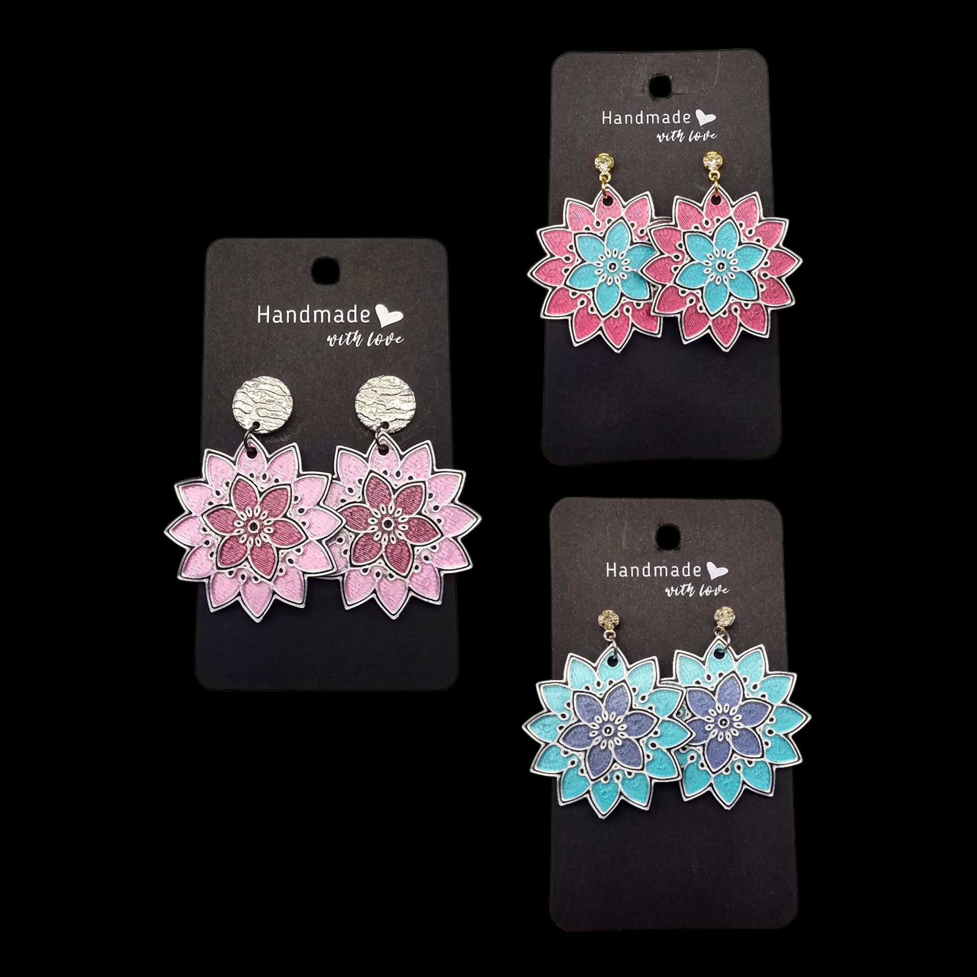 Drie paar handgemaakte bloemvormige oorbellen in roze, roze-blauwgroen en blauwgroen-paars, gepresenteerd op zwarte kaartjes.