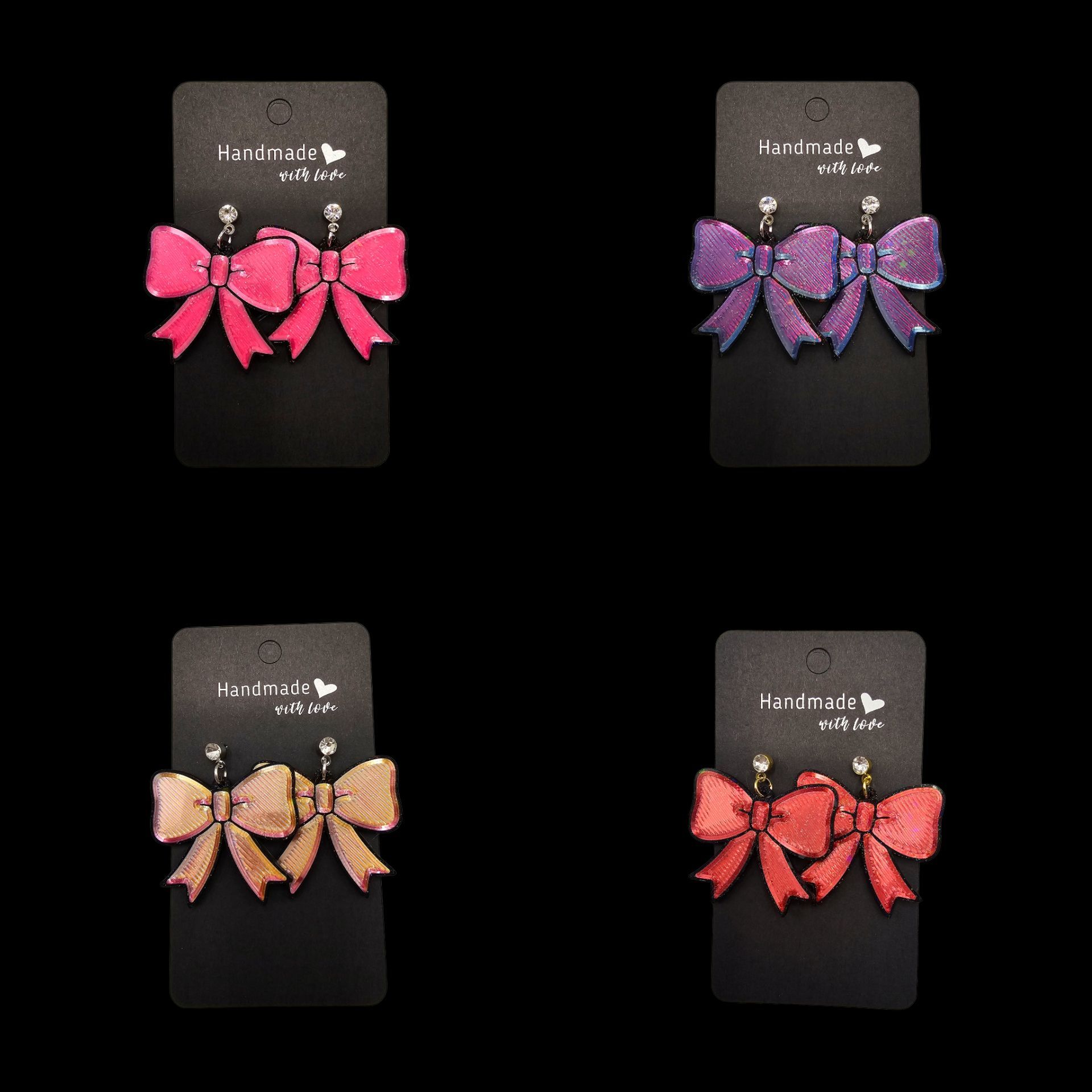Vier paar strikvormige oorknopjes in roze, paars, goud en rood, elk gepresenteerd op een zwart