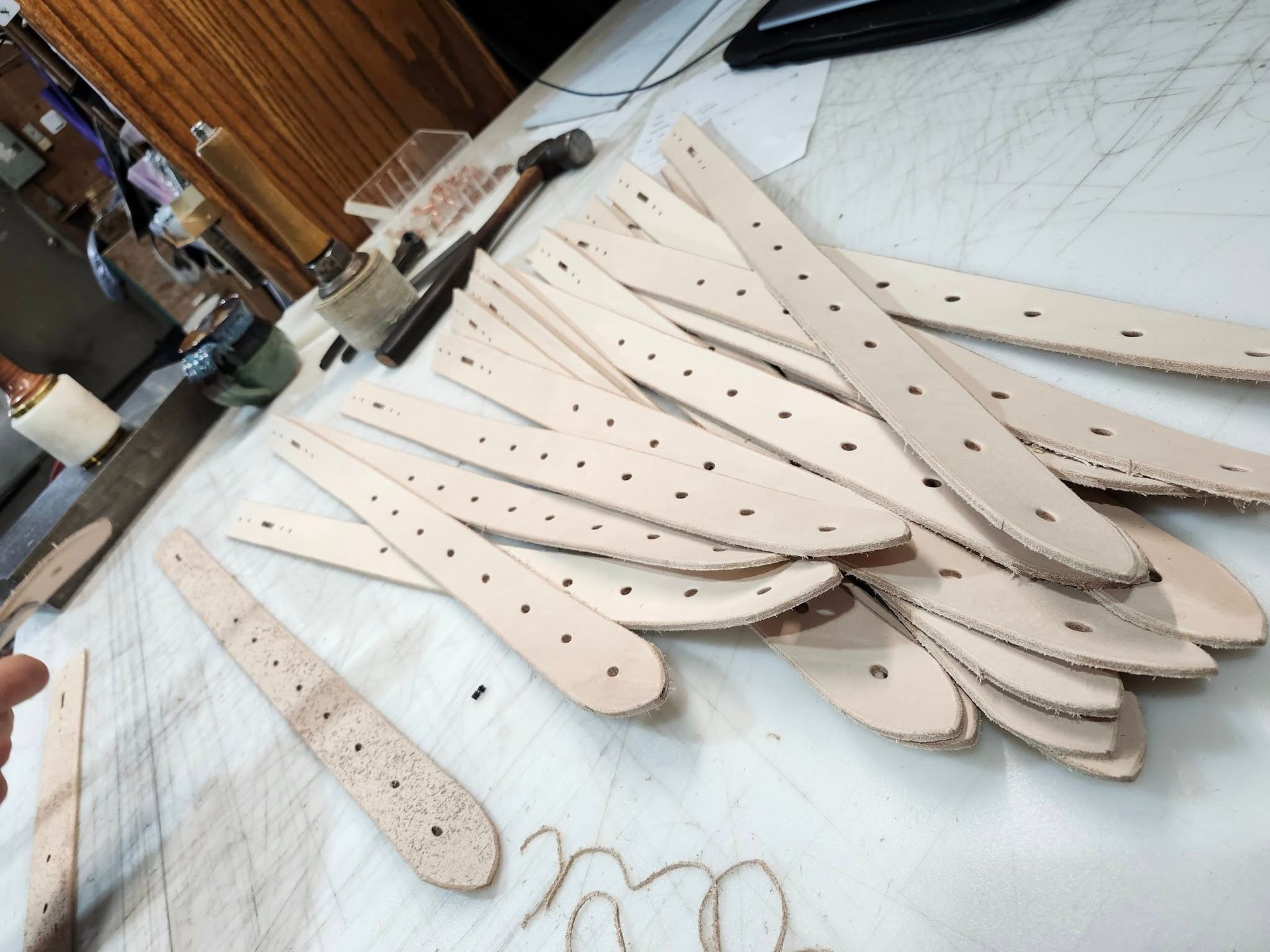 A pile of light tan leather strips with pre-punched holes laid out on a workshop table.