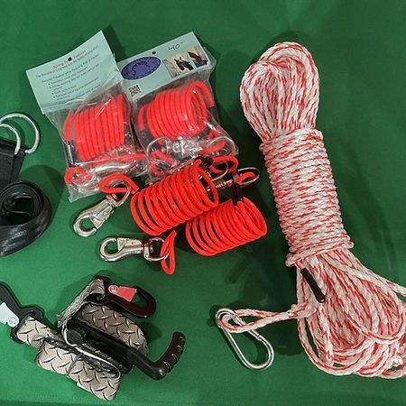 Several pieces of orange coiled tether cords with metal clips, a long white and red rope, and various hardware accessories.