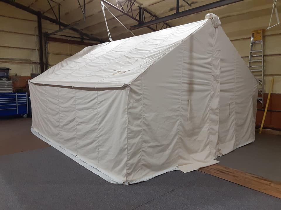 A white, rectangular frame tent set up indoors on a grey floor in a workshop or warehouse.