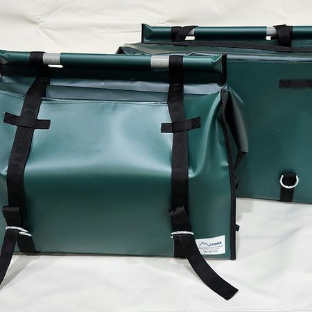 Two dark green, waterproof roll-top pannier bags with black straps and buckles against a white background.