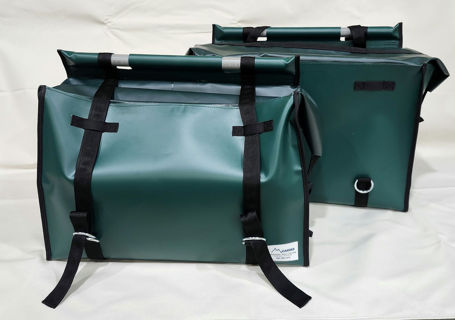 Two dark green, rectangular, roll-top storage bags with black buckle straps against a plain, off-white background.