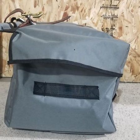 A gray, rectangular gear bag with a black trim and webbing strap, sitting on a light surface against a wood-paneled wall.