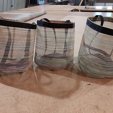 Three woven, multi-colored baskets with black fabric rims sit in a row on a wooden workshop surface.