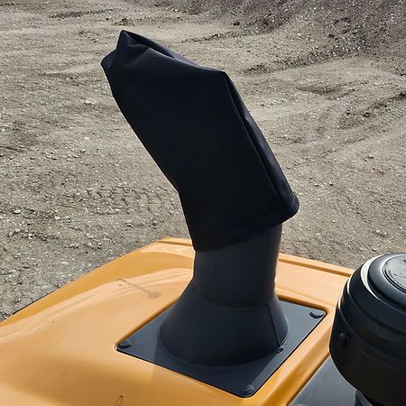 A black fabric rain cap cover on a vertical exhaust pipe of yellow construction equipment on a gravel site.