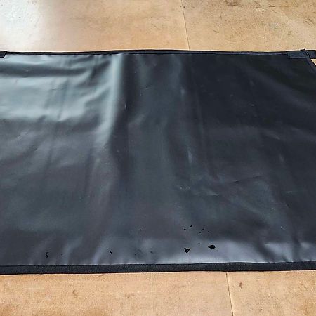A rectangular, black vinyl mat with a textured border lies flat on a light-colored, concrete-like floor.