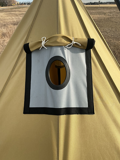 A tan canvas tent featuring a square, fire-resistant stove jack patch with a circular opening, set in an outdoor field.