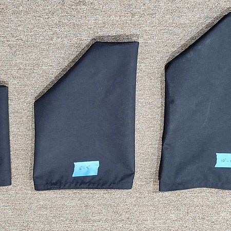 Three black, rectangular fabric covers of varying sizes arranged horizontally on a textured surface.
