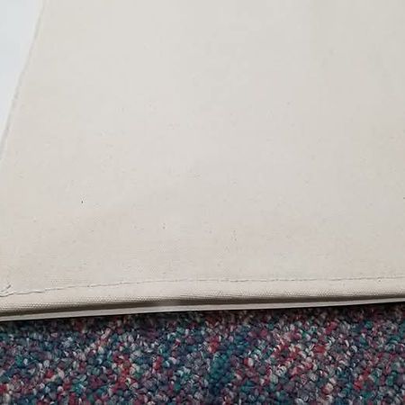 A close-up view of a beige fabric edge with stitching, resting on a textured, multicolored patterned carpet.