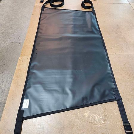 A rectangular black vinyl equipment cover or heavy-duty sling with black nylon straps and buckles at the corners.