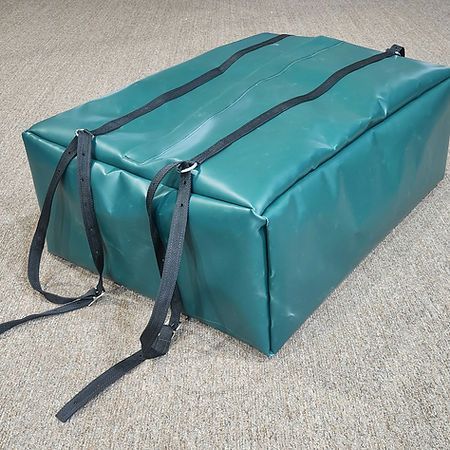 A rectangular, dark green, vinyl-covered storage bag featuring two black nylon straps with buckles, sitting on a rug.