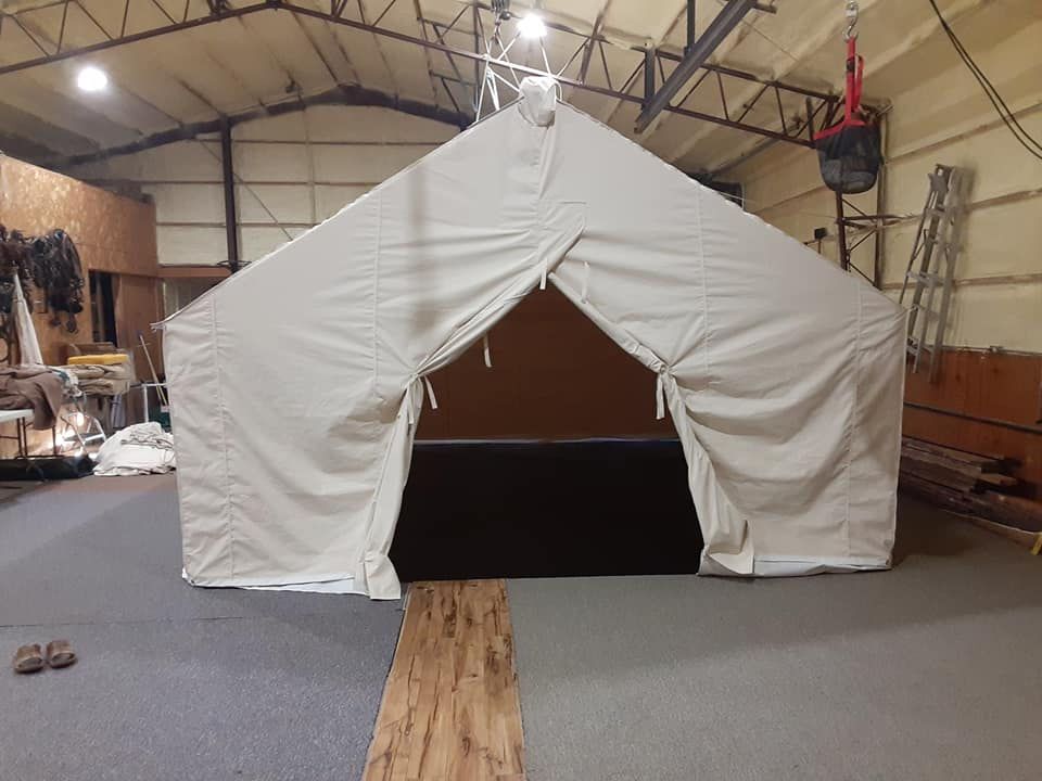 A large, beige canvas tent frame set up indoors, with its two-panel door flaps tied open.
