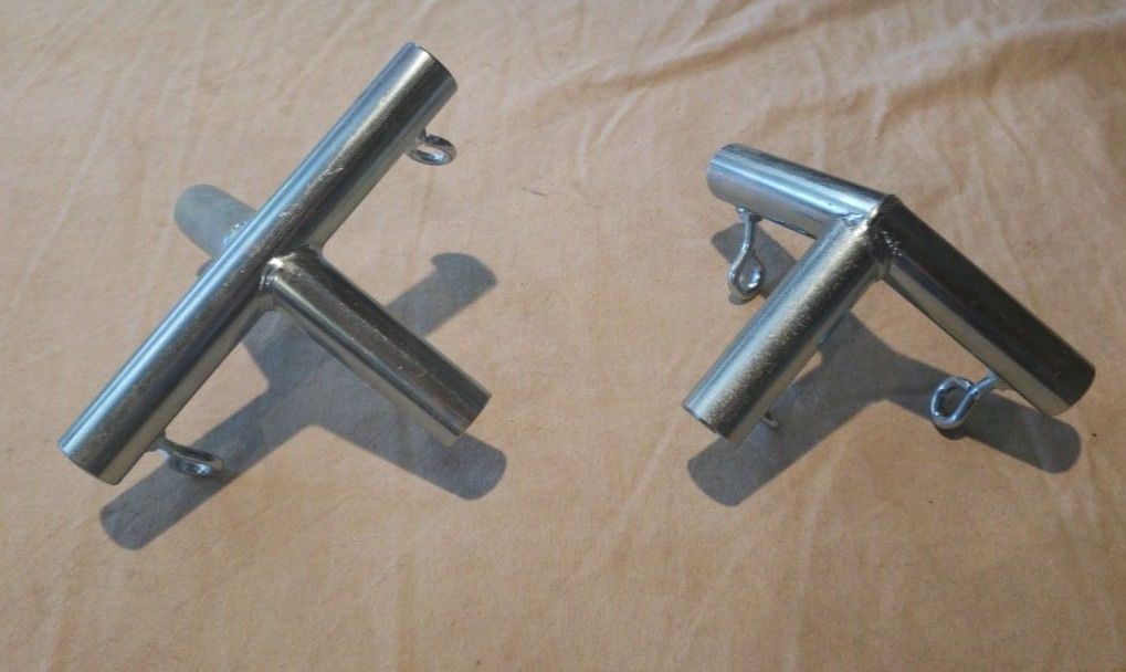 Two stainless steel pipe connectors with small eye bolts, displayed on a tan surface.