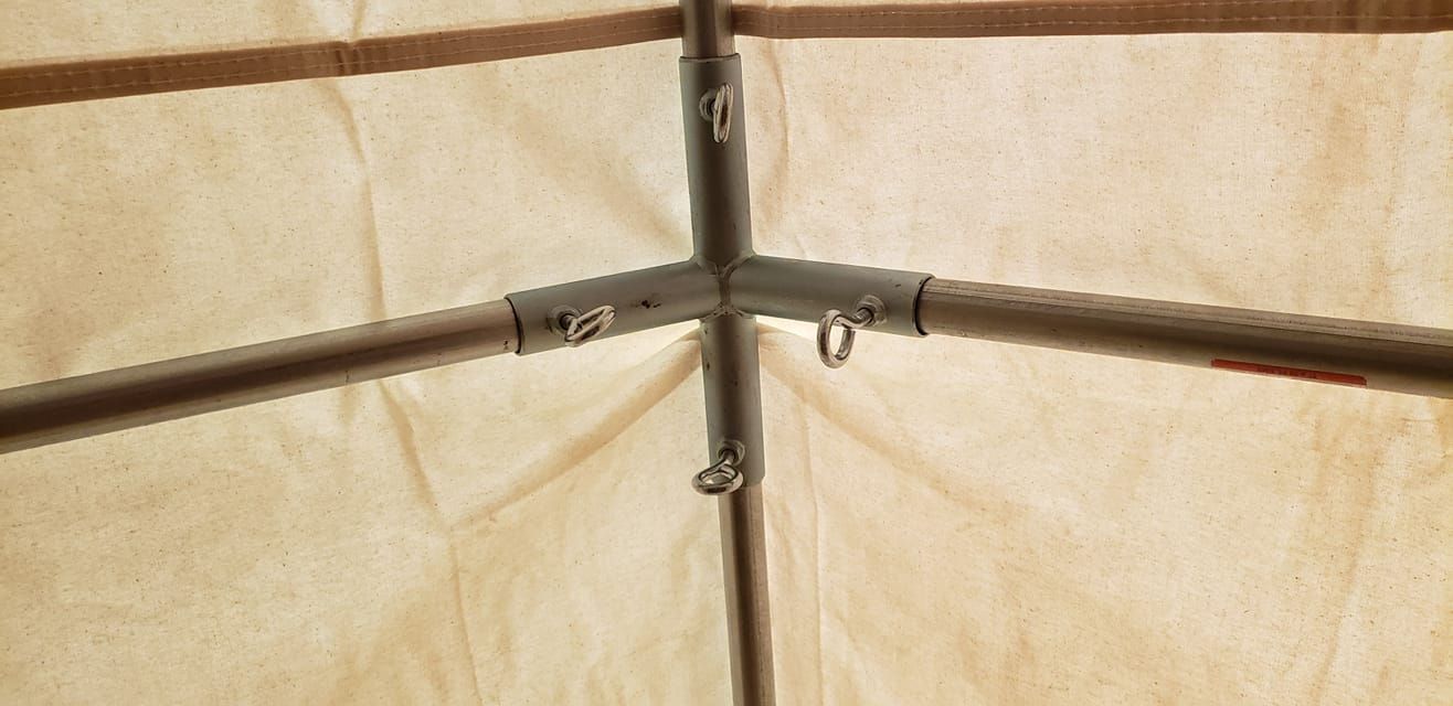 A beige fabric tent ceiling showing a central metal corner joint connecting three pole segments with silver rings.
