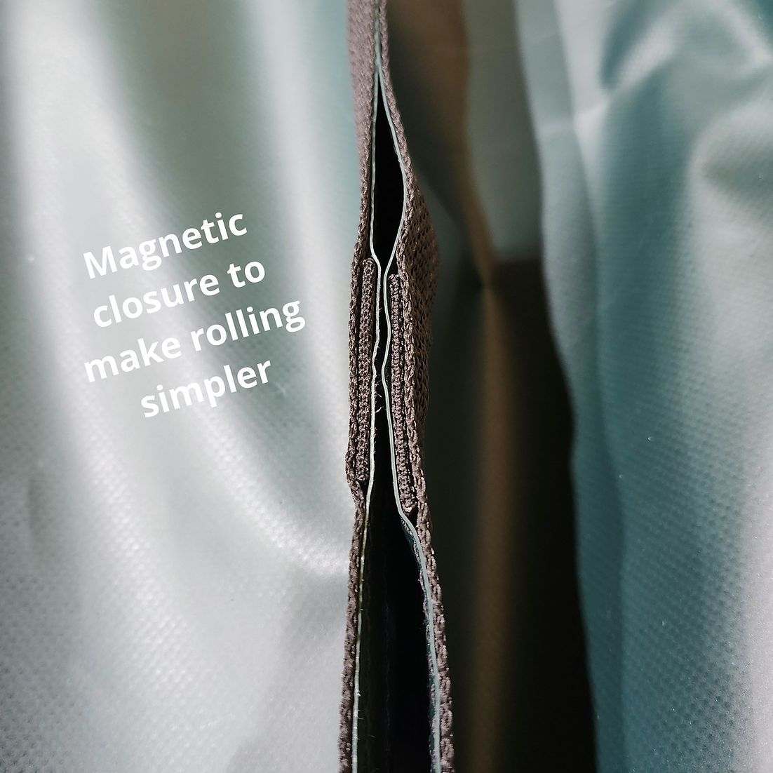 A close-up of a brown, textured magnetic fabric closure on a smooth, pale blue material to assist with rolling.
