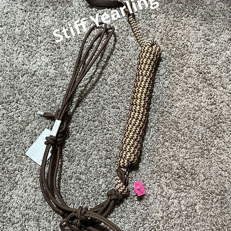 A brown rope halter for a yearling, featuring a braided tan and brown noseband, laid against a gray carpet background.