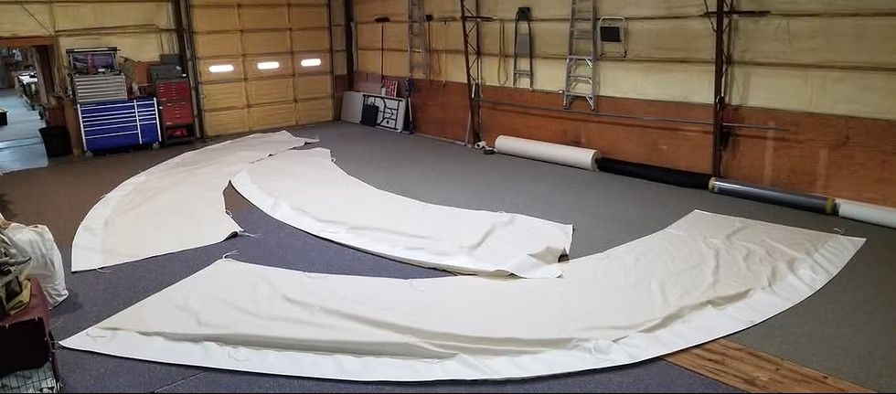 Three large white canvas sail panels laid out on the floor of a spacious industrial workshop.