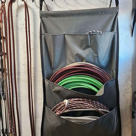 A gray, multi-pocket wall organizer hangs on a wall, holding several coiled ropes, with long reins hanging to the left.