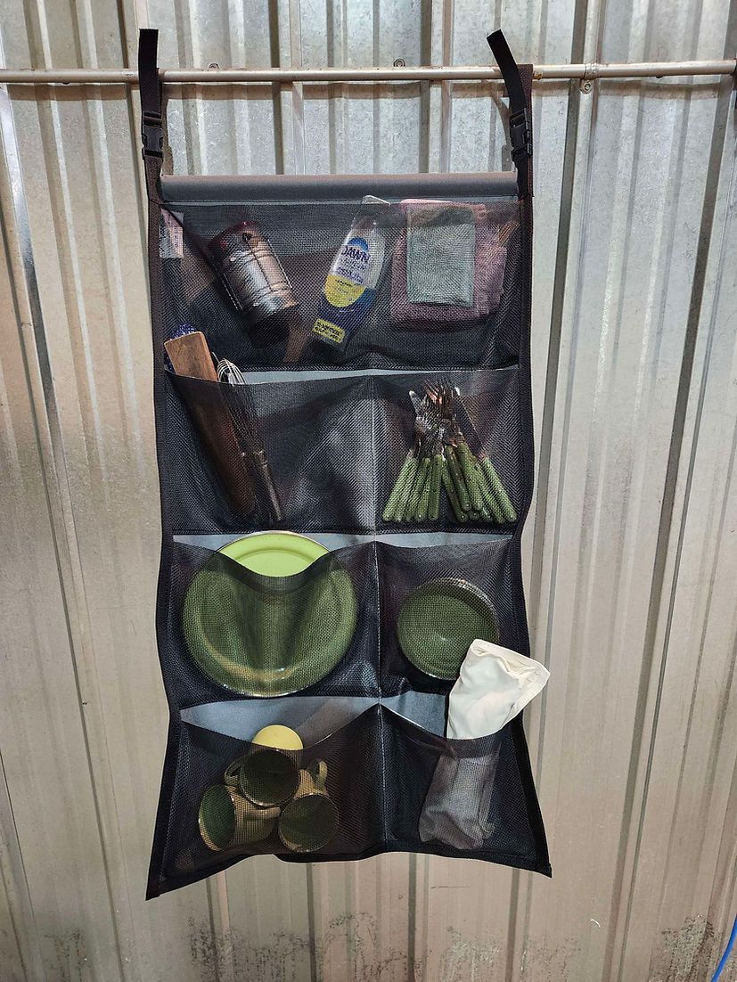 A black hanging organizer with multiple mesh pockets filled with assorted tools and household items on a metal wall.