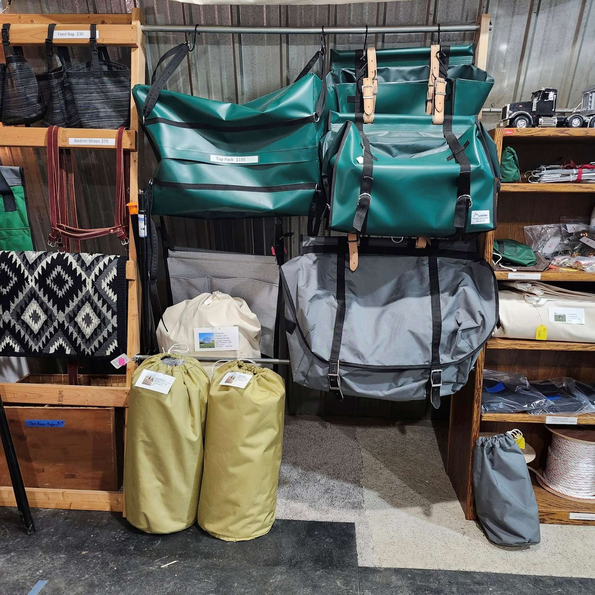 Various canvas bags, including green, grey, and tan models, are displayed on hangers and shelves in a shop.